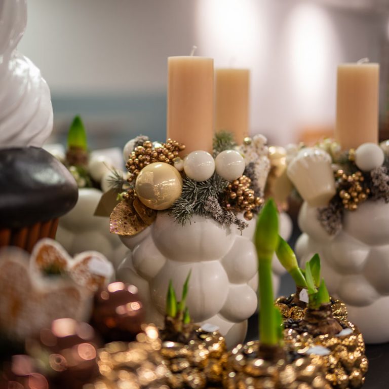 Weiße Kugelvasen mit Amaryllis, goldener Dekoration und beigen Stumpenkerzen