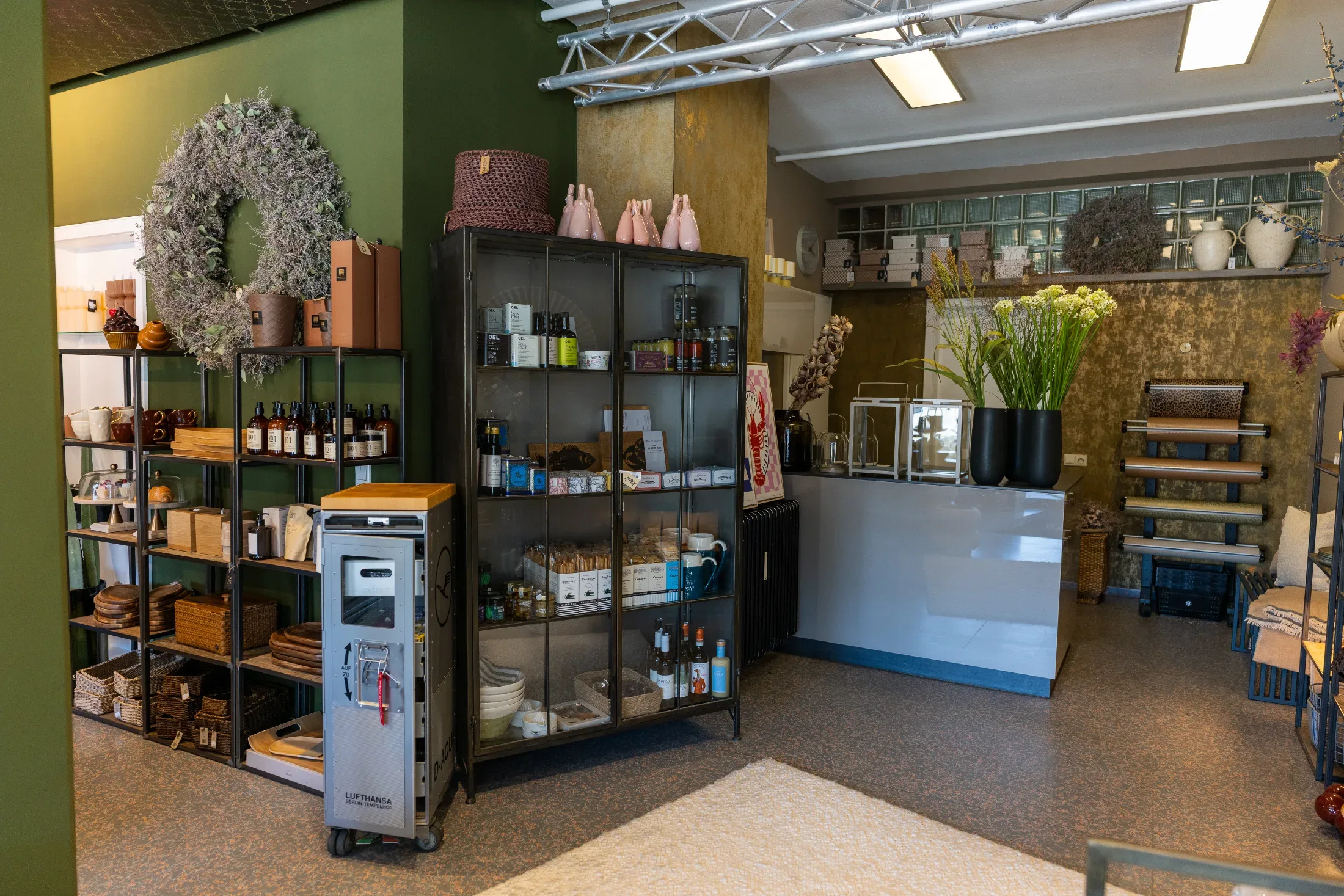 Glasvitrine mit Ölen und Feinkost neben Kasse und Geschenkpapierrollen