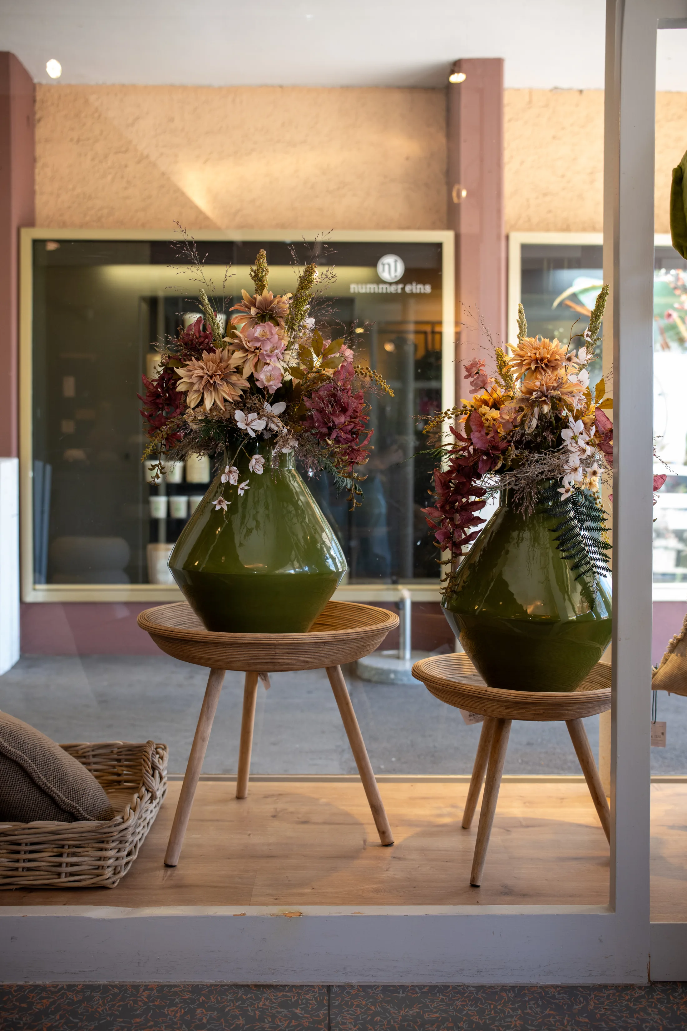 Zwei grüne Bodenvasen mit großen Blumensträußen auf Holzhockern im Schaufenster
