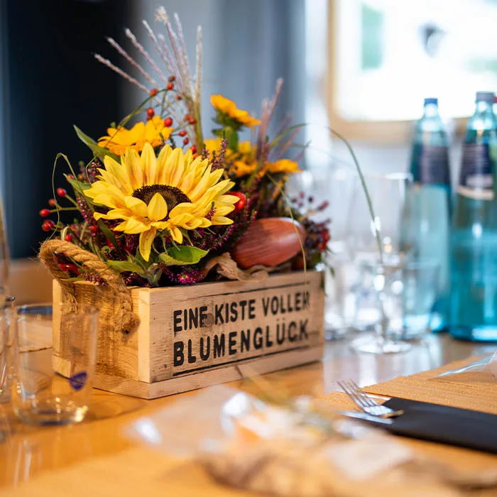 Holzkiste mit Sonnenblumen und Beeren als Tischdekoration, darauf „Eine Kiste voller Blumenglück“