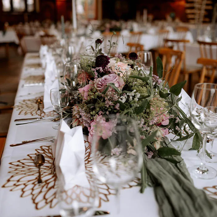 Lange Hochzeitstafel mit Rosen, Schleierkraut und grünem Tischläufer zwischen Weingläsern