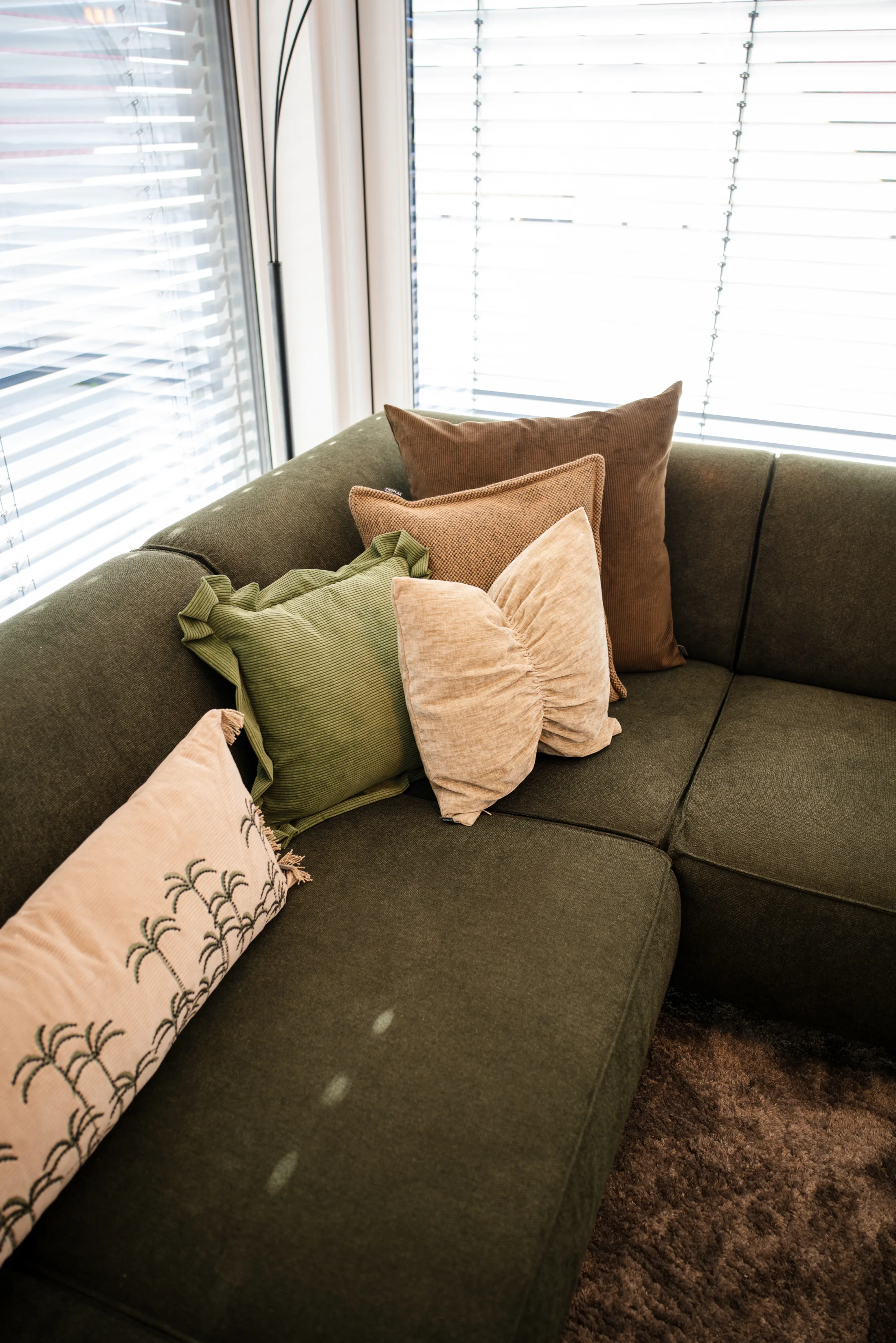 Kissen in Olivgrün, Creme und Braun auf dem Ecksofa vor dem Fenster