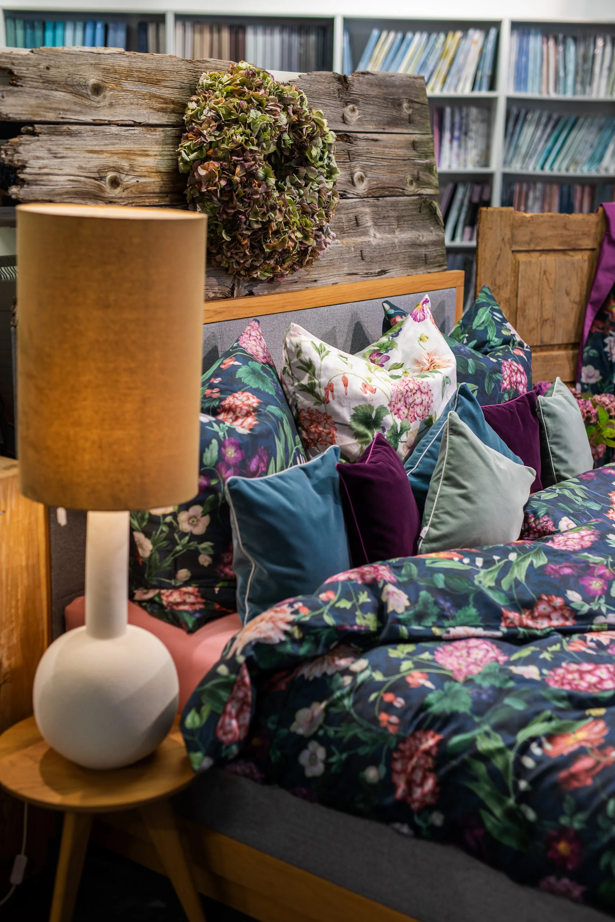 Tischleuchte mit Keramikfuß neben einem Bett voller Kissen mit Blumenmuster