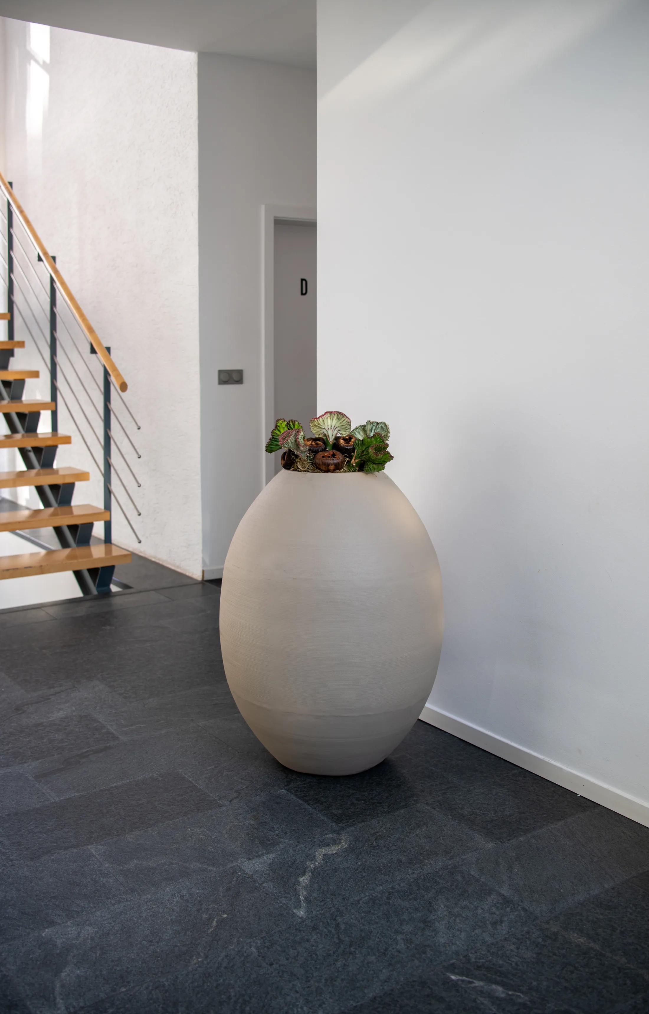 Große helle Bodenvase mit Sukkulenten im Eingangsbereich vor der Treppe