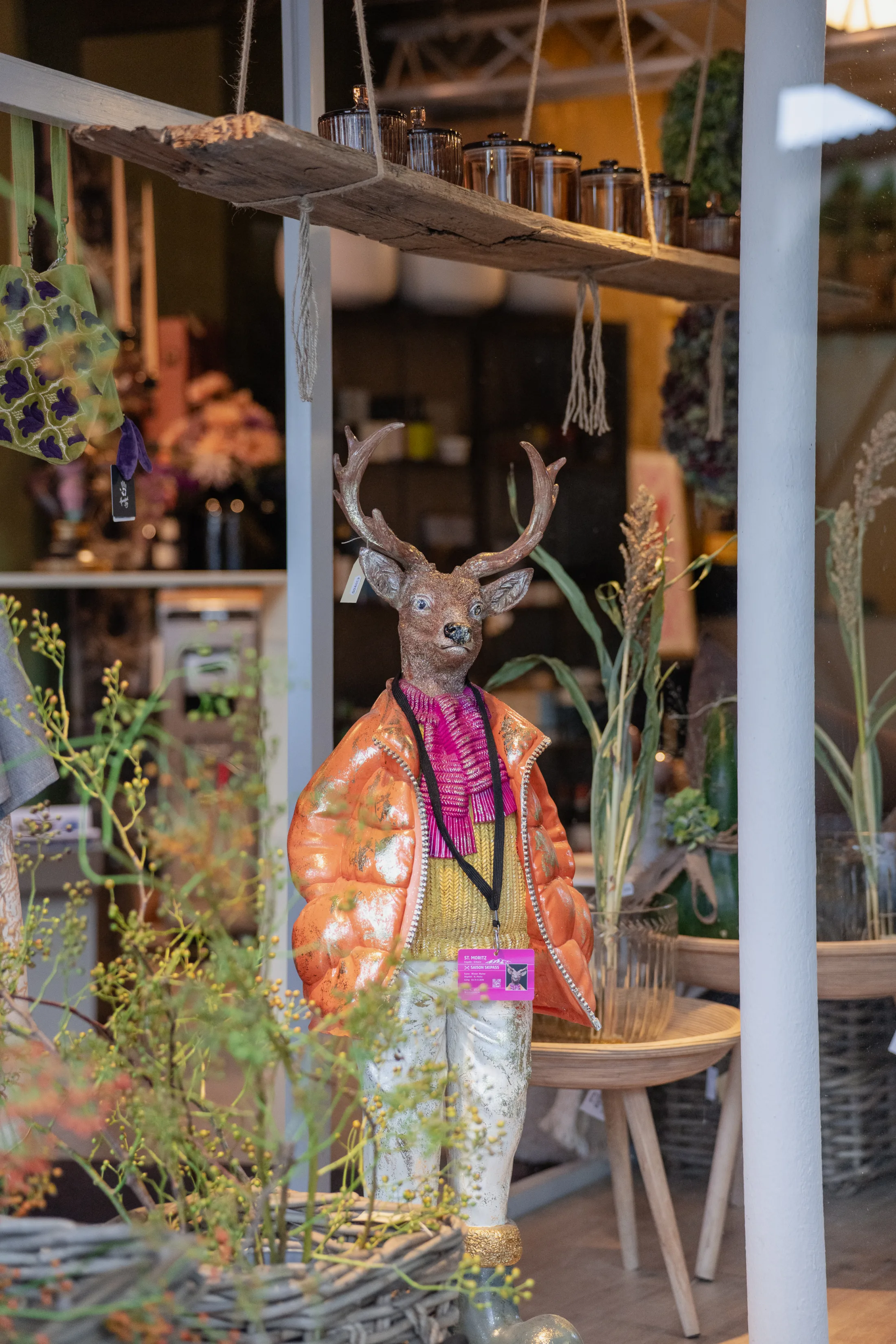 Hirschfigur mit orangefarbener Daunenjacke und pinkem Schal zwischen Gräsern