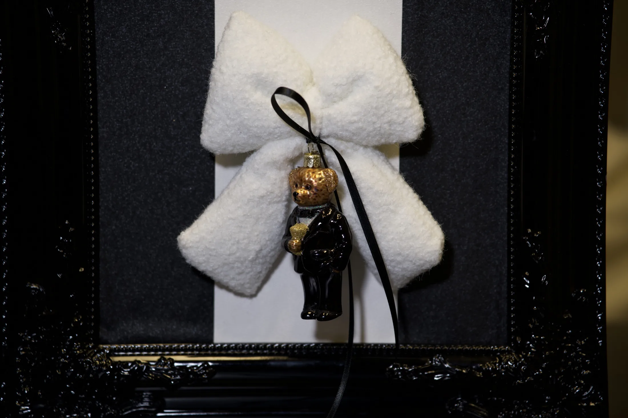 Weiße Plüschschleife mit schwarzem Band und einem Teddy im Smoking, nah